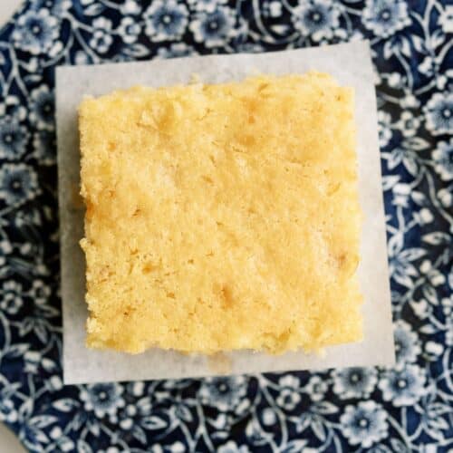 A square piece of cornbread sits on a white paper atop a blue and white floral-patterned plate.