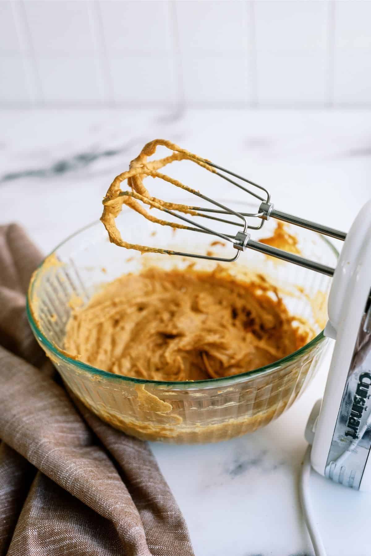 Pumpkin filling mixed with a hand mixer in a glass bowl