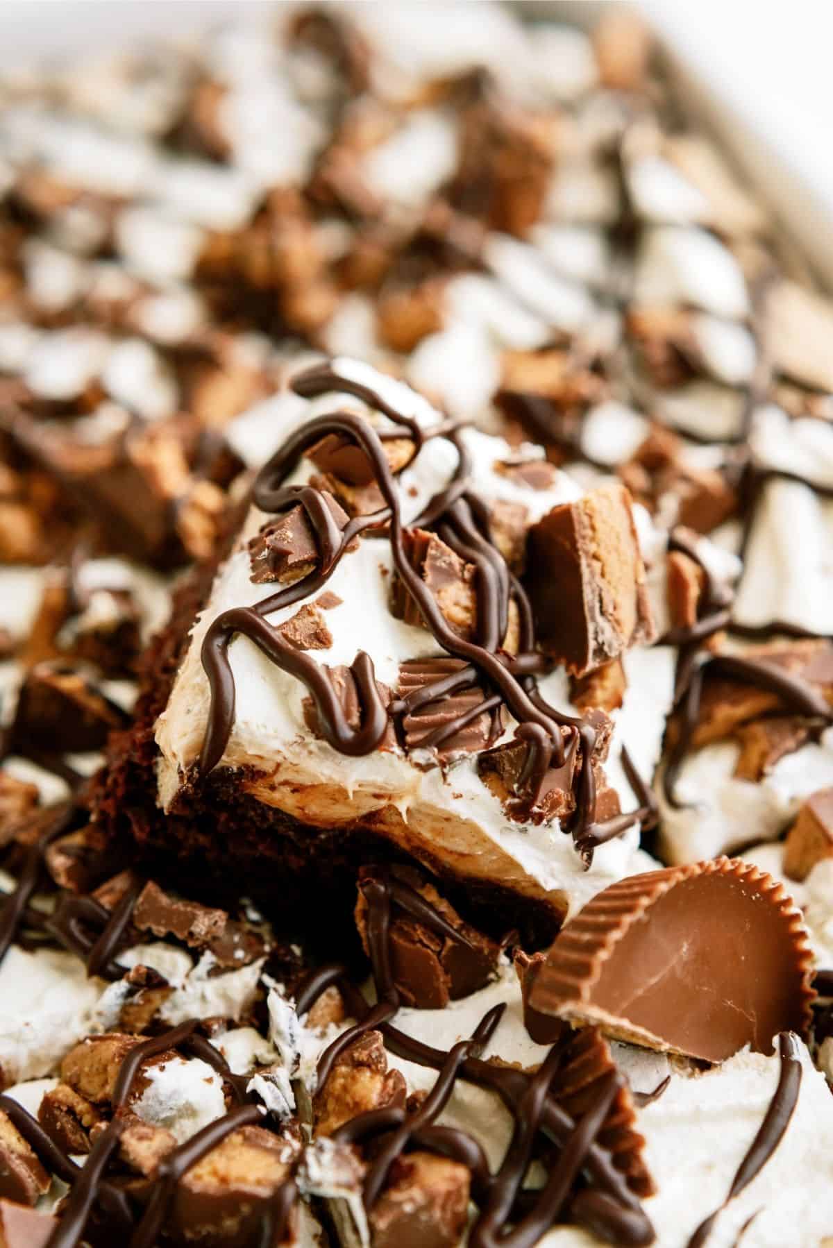 A slice of Reese’s Peanut Butter Poke Cake over the pan of Reese’s Peanut Butter Poke Cake