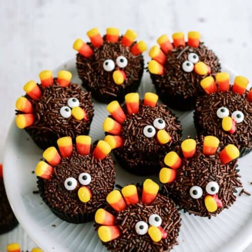 Chocolate cupcakes decorated to resemble turkeys, with candy corn feathers and candy eyes, arranged on a white plate.
