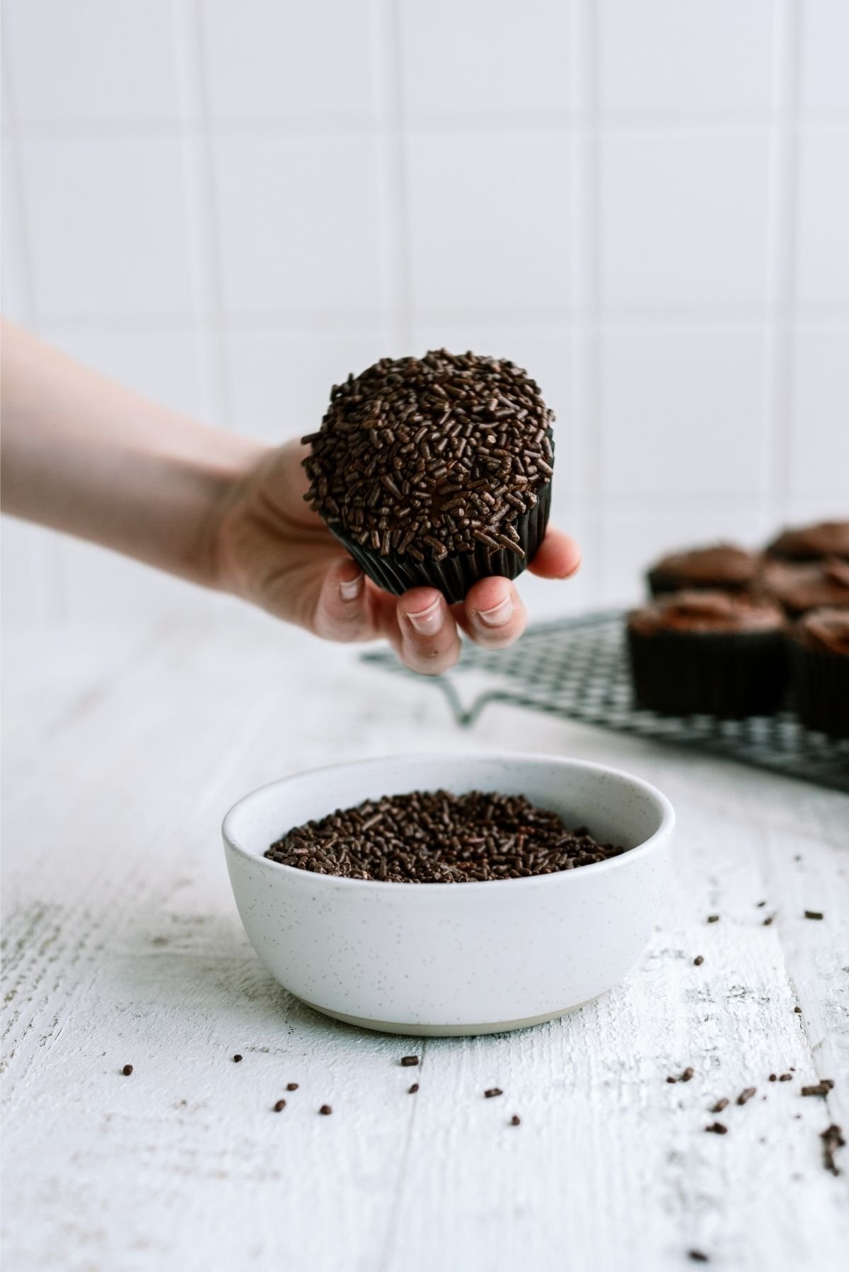 Chocolate cupcake with frosting dipped into a bowl of chocolate sprinkles