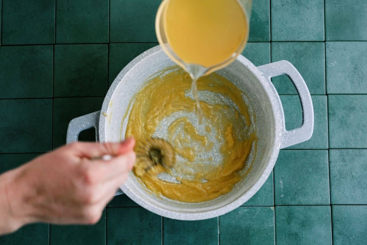 Adding Chicken broth to the enchilada sauce mixture in the pan