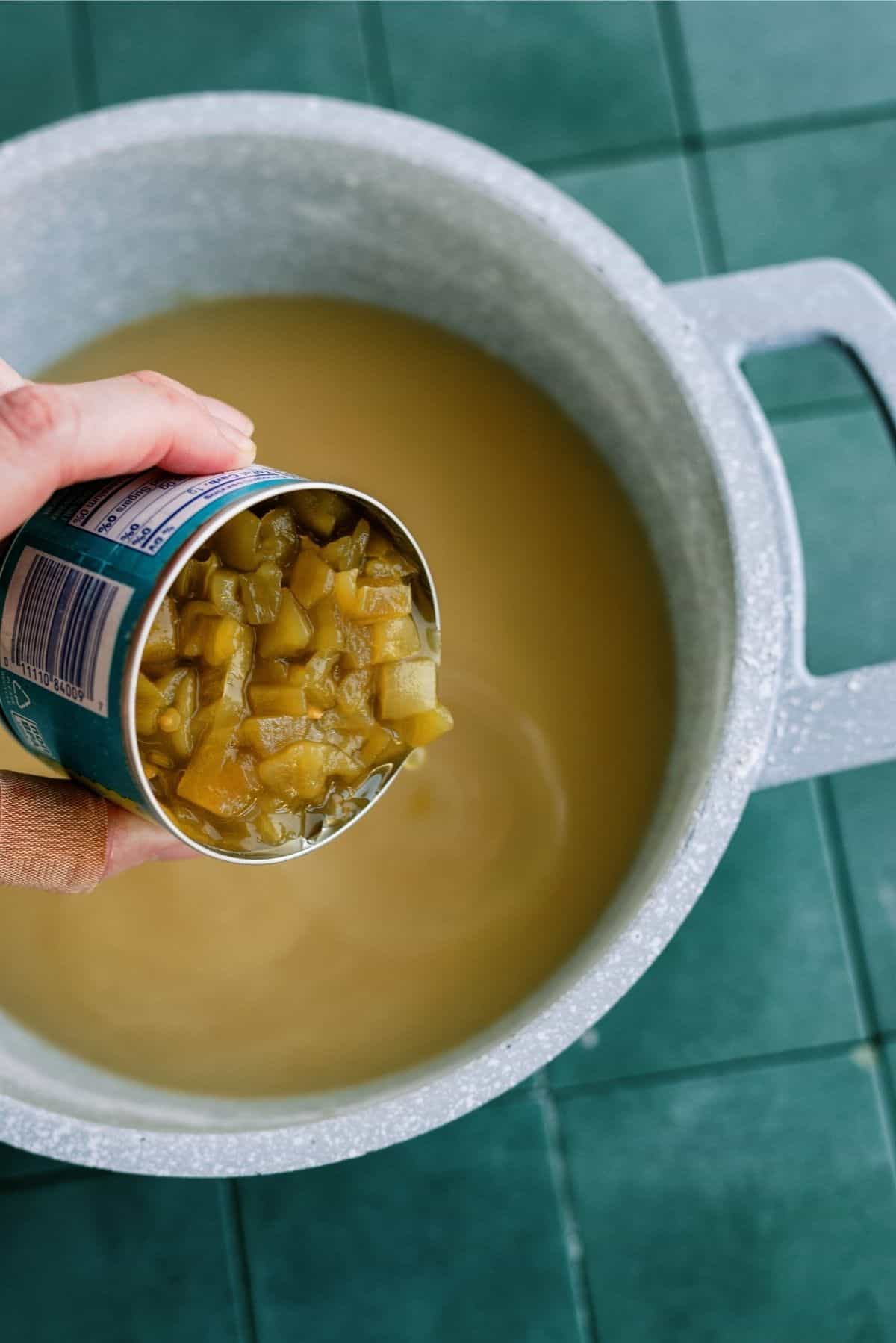 Adding a can of diced green chilies to enchilada sauce in pan