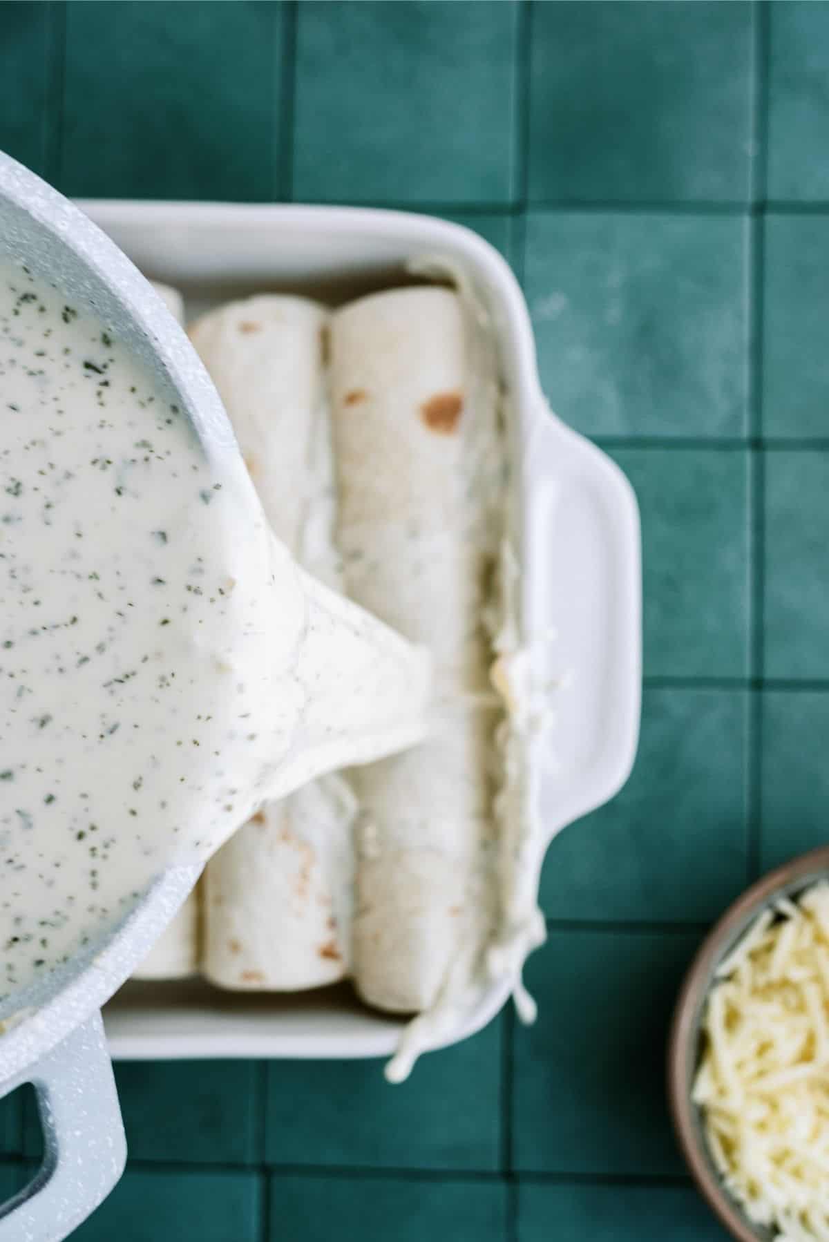 Pouring enchilada sauce over tortillas in baking pan