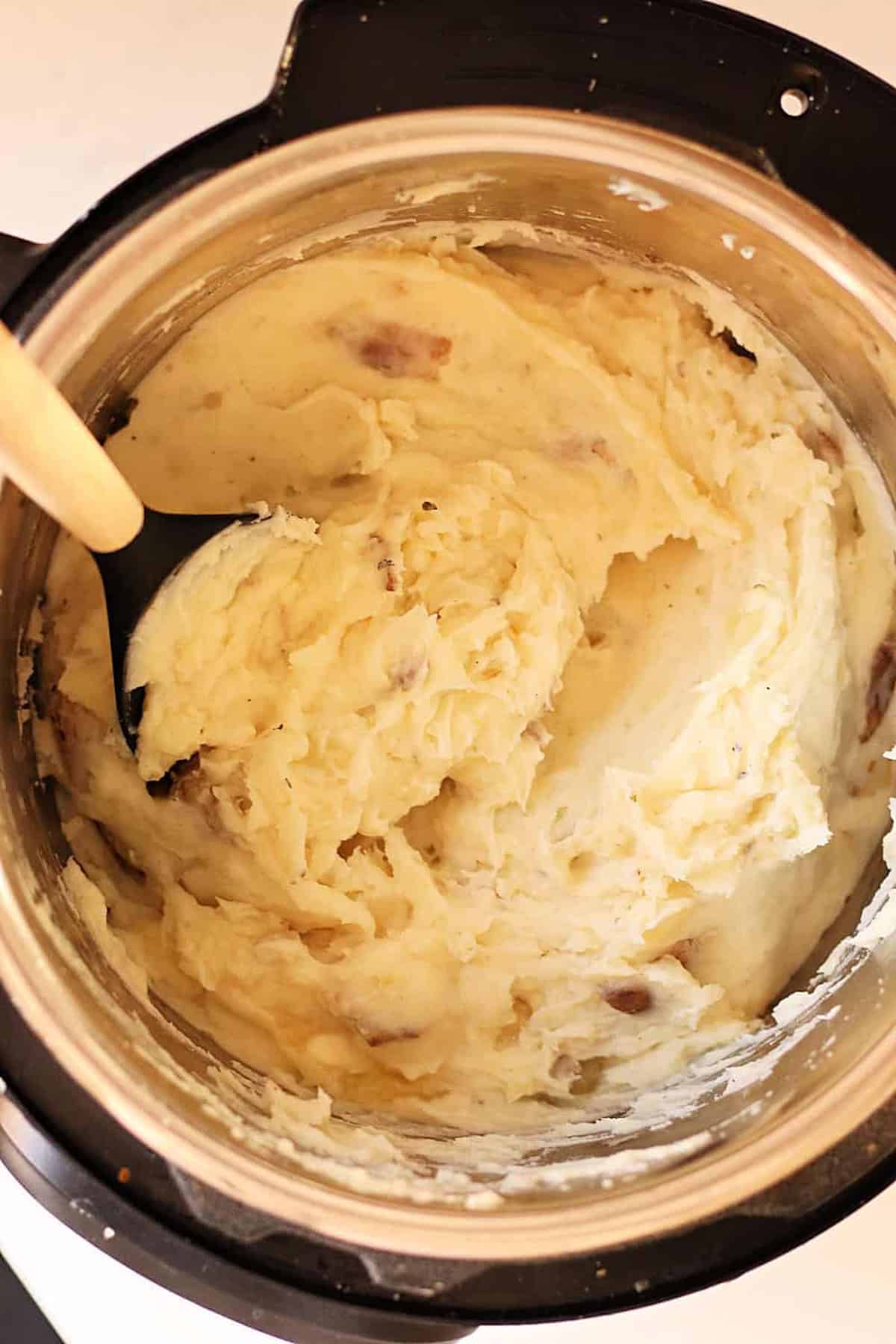 A pot of mashed potatoes with bits of potato skin, being stirred with a black spoon.
