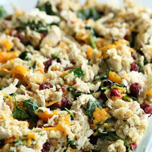 A close-up of a casserole dish filled with a mixture of shredded turkey, greens, cheese, cranberries, and stuffing mix.