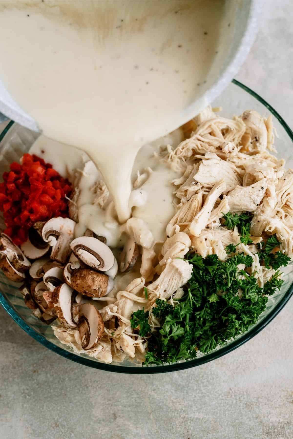 Pouring cream sauce on top of ingredients in glass mixing bowl