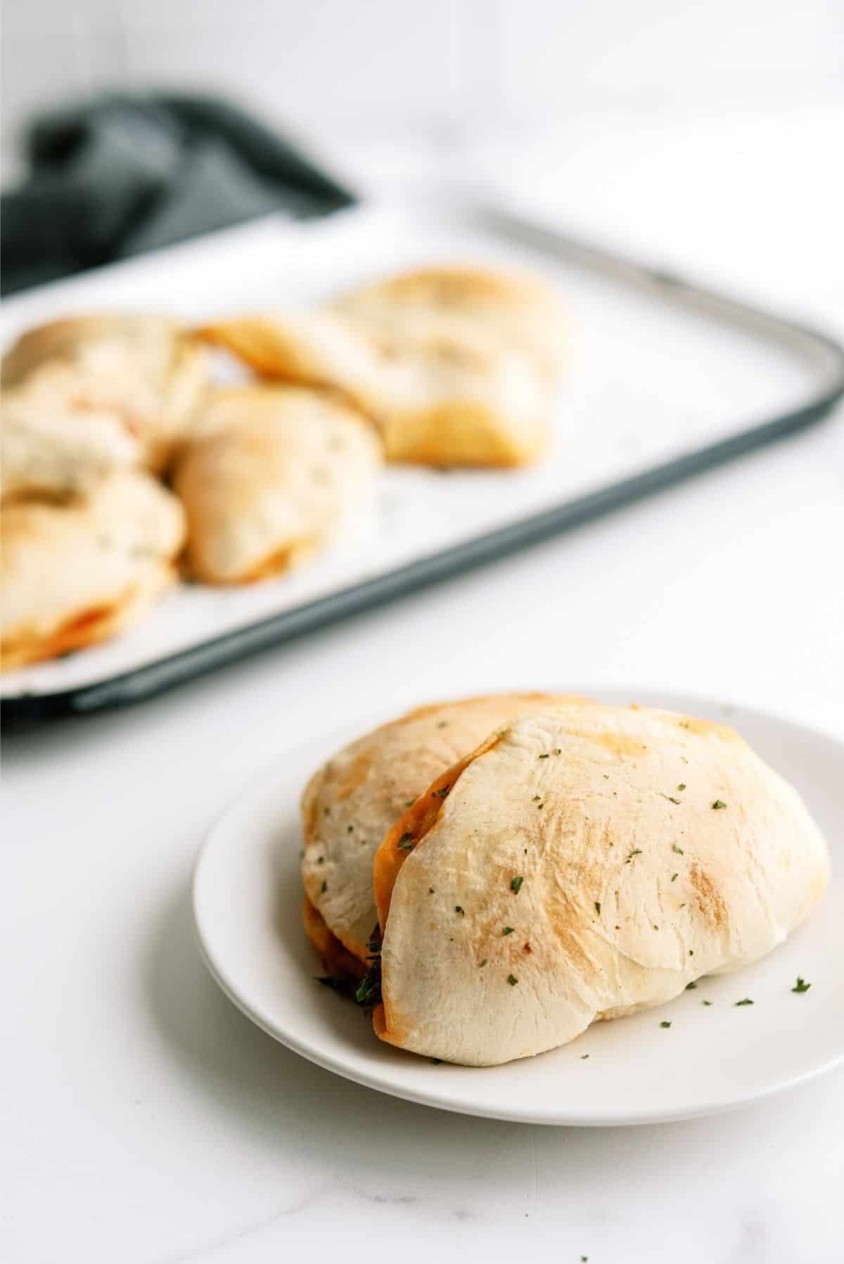 Homemade Pizza Pockets on a plate with a sheet pan of pizza pockets in the back