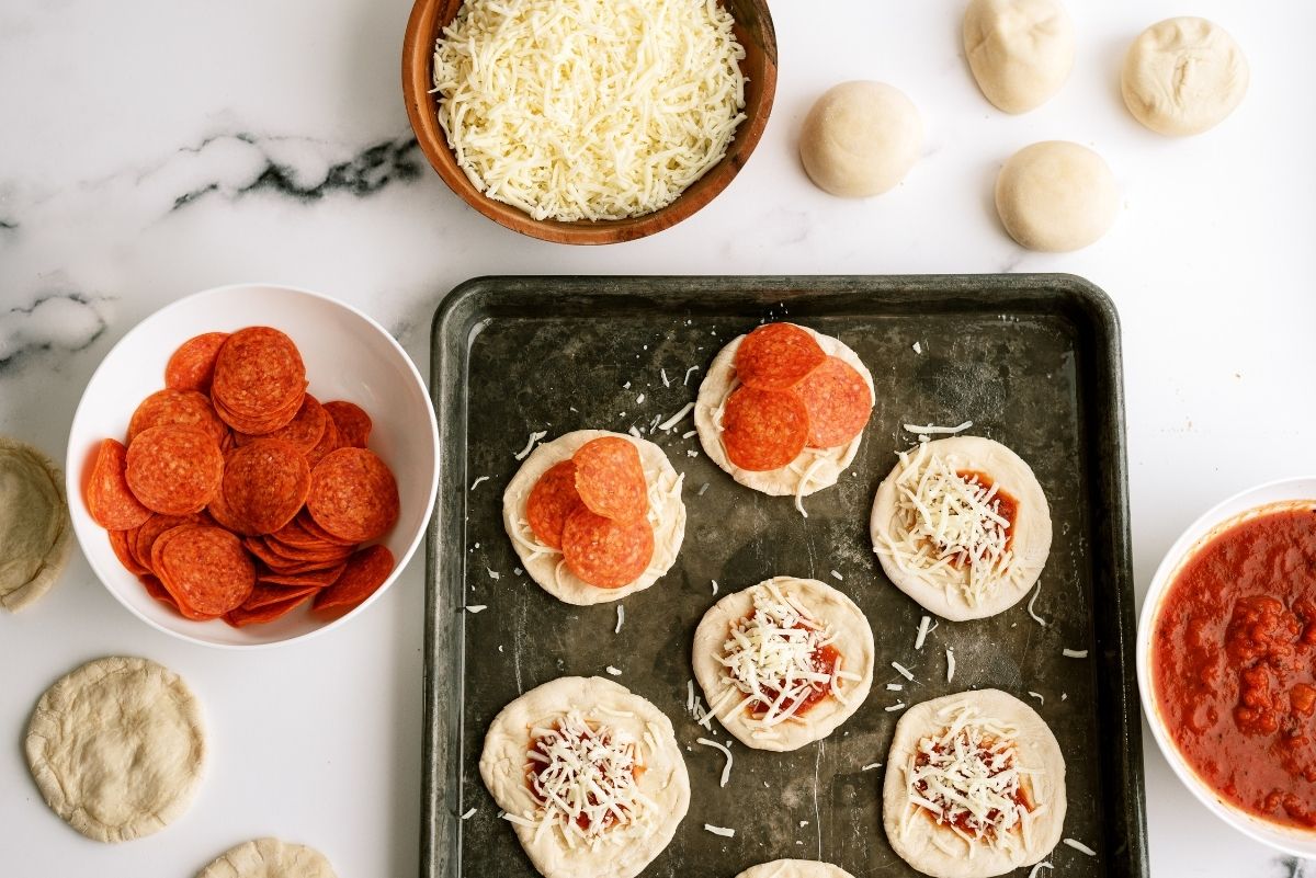 Pizza sauce, cheese and toppings added to dough on sheet pan