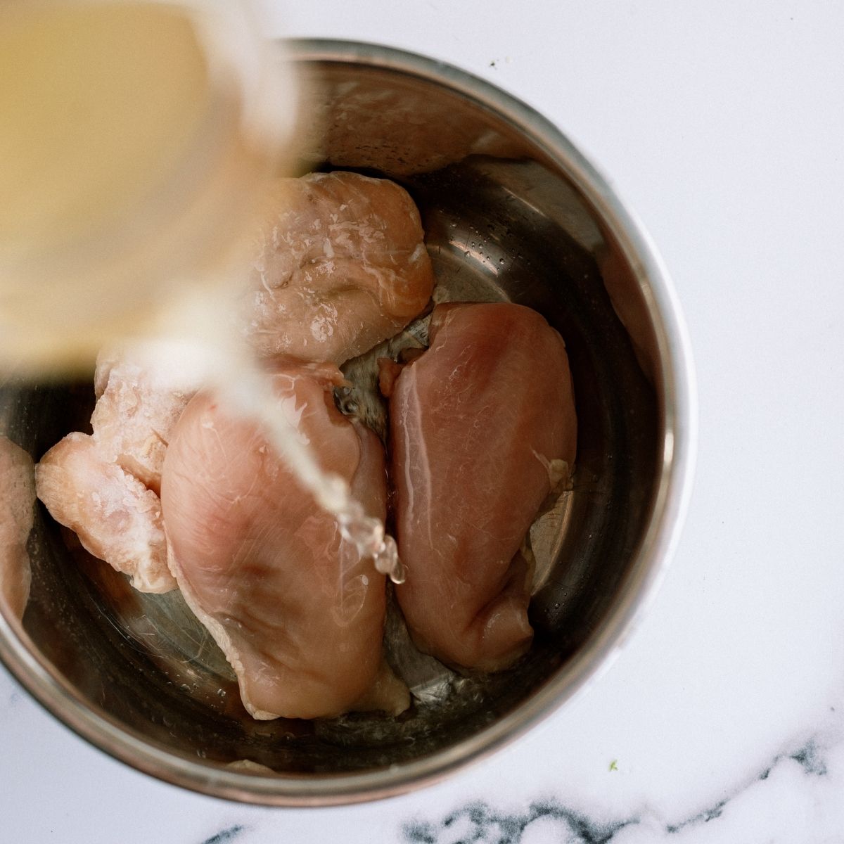 Pouring chicken broth over chicken in instant pot