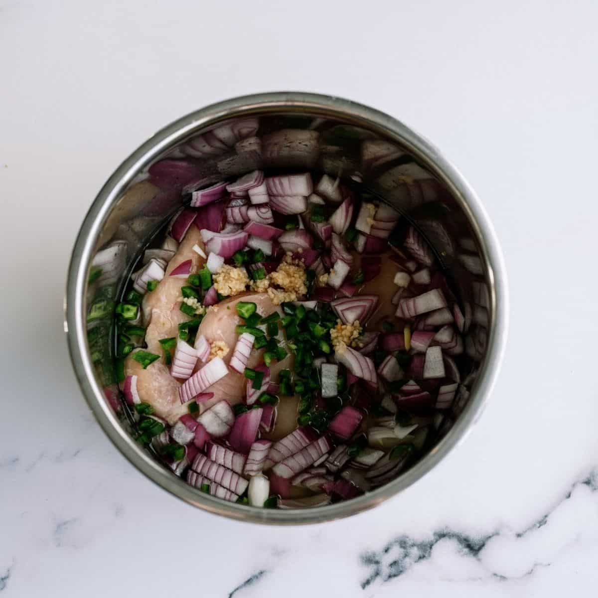 Chopped onion and jalapeno on top of chicken in Instant Pot