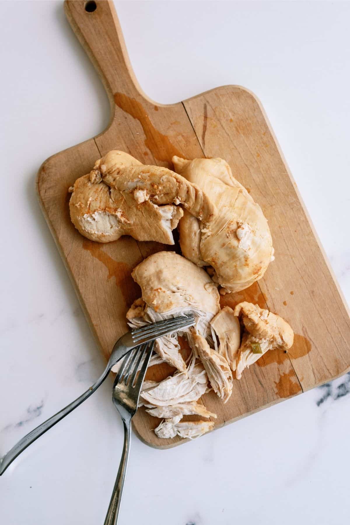 Cooked Chicken on cutting board with 2 forks shredding it