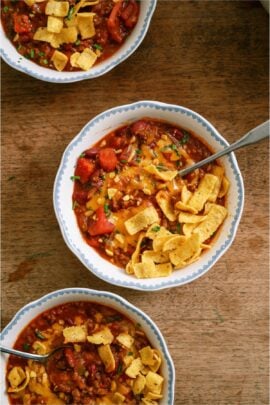 3 bowls of Mom's Crockpot Chili with one in the center with a spoon topped with corn chips.