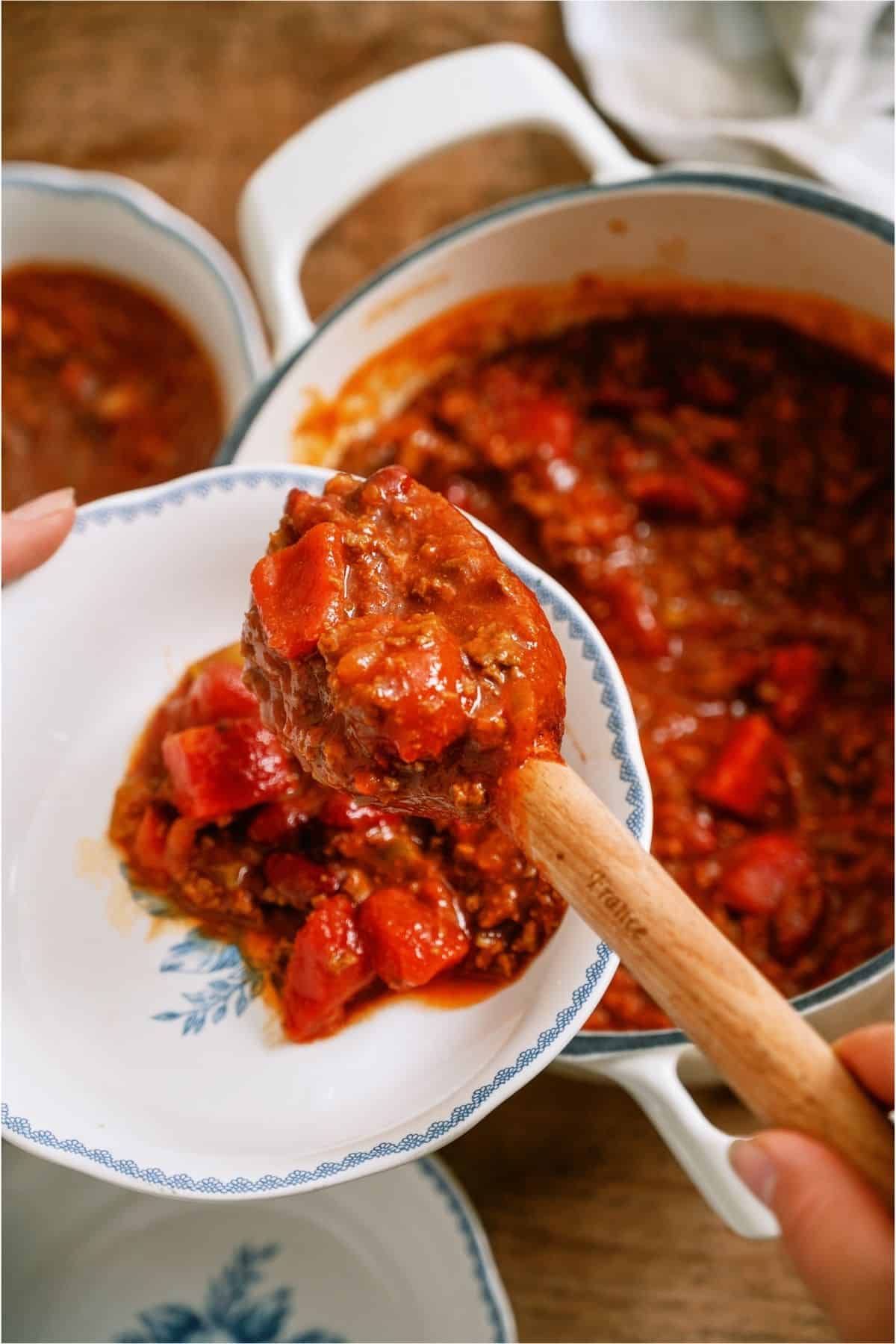 A wooden spoon spooning a serving of Mom's Crockpot Chili into a bowl.