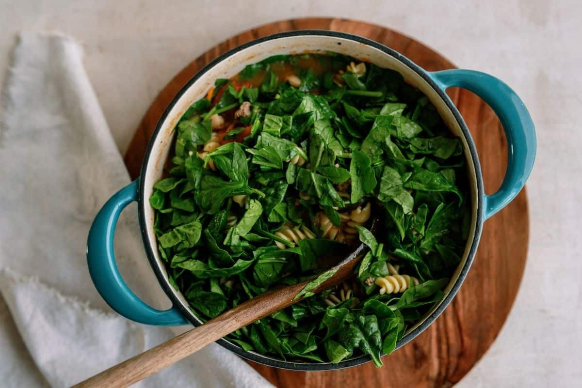 Spinach in the stock pot stirred with a wooden spoon