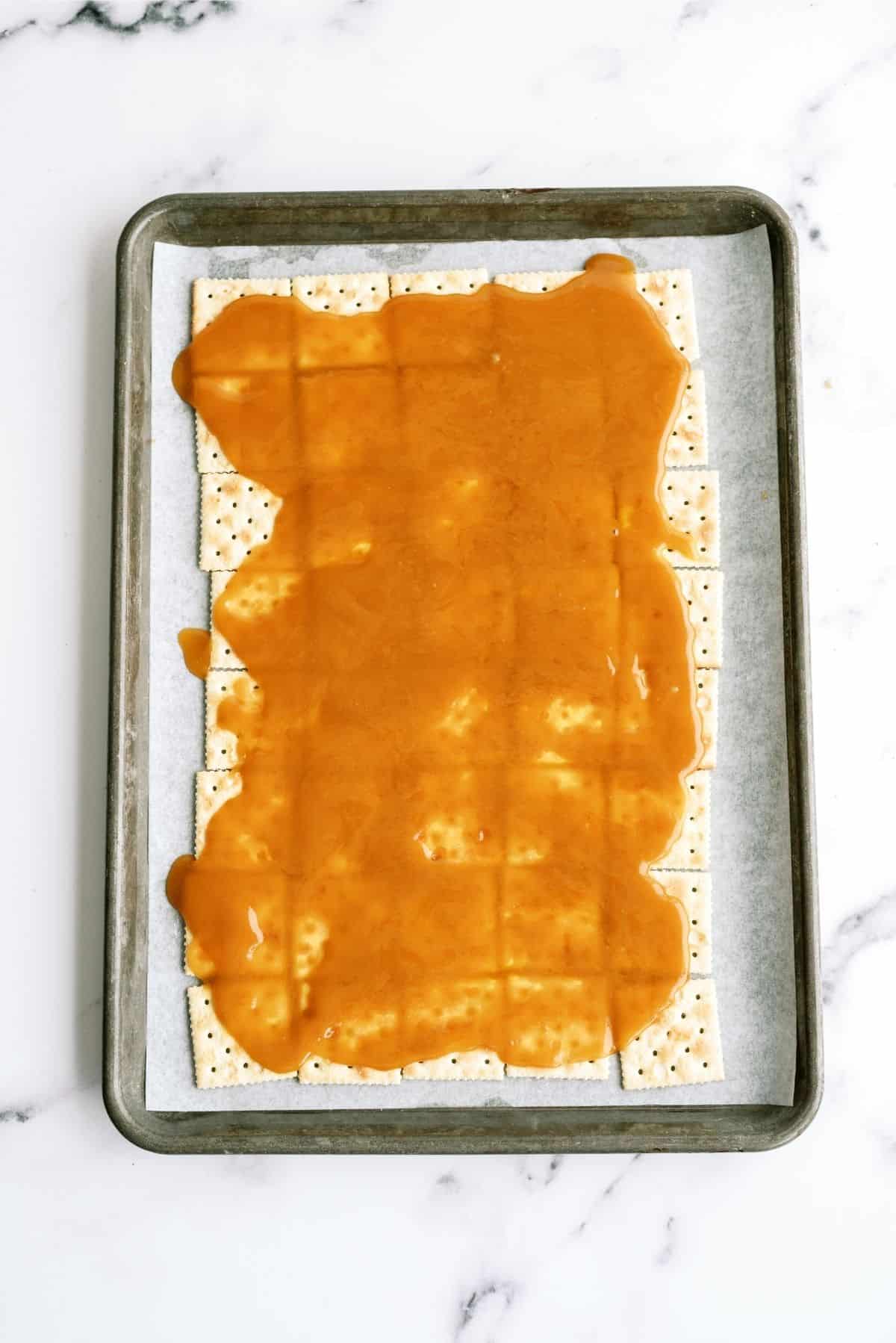 Butter and Brown sugar mixture poured over saltine crackers on a baking sheet lined with parchment paper.