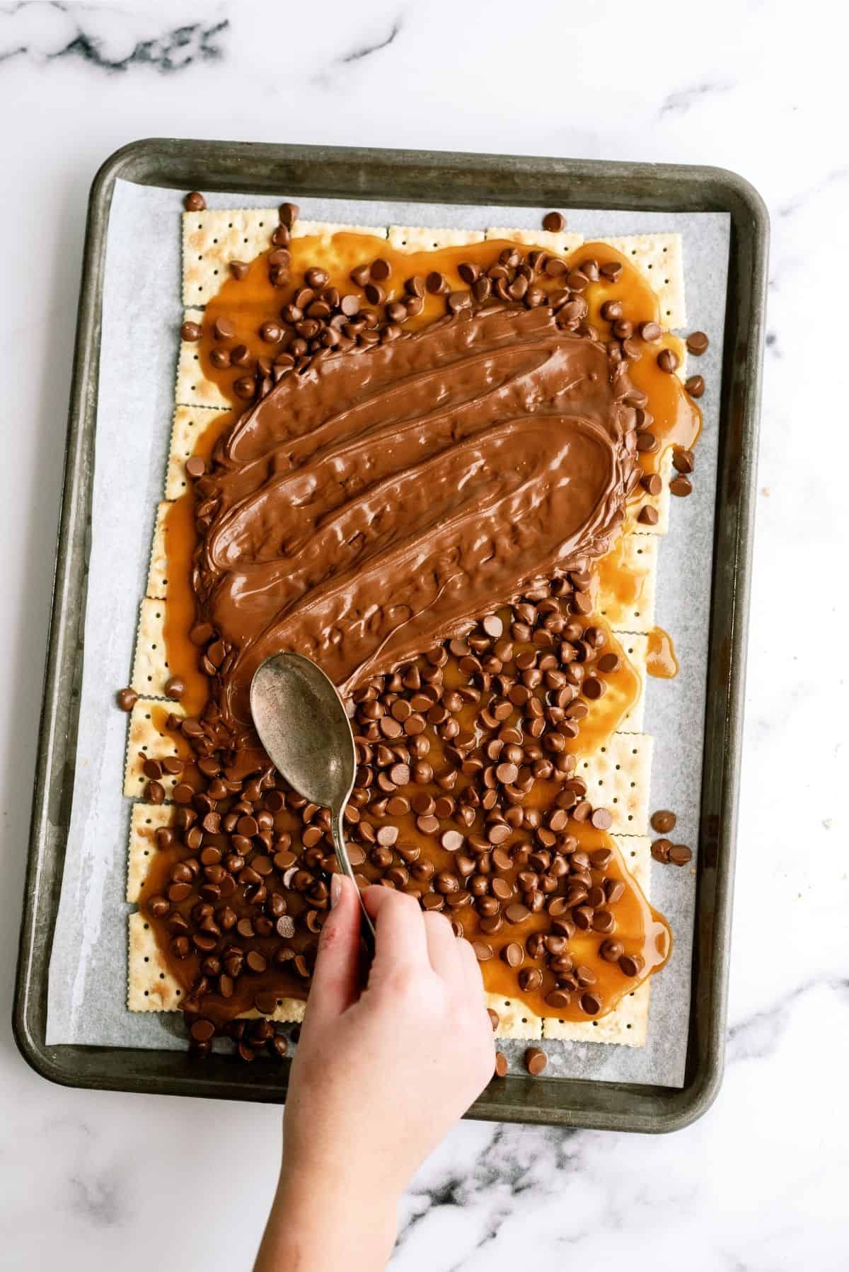Spreading chocolate chips melted on top of brown sugar and butter layer.