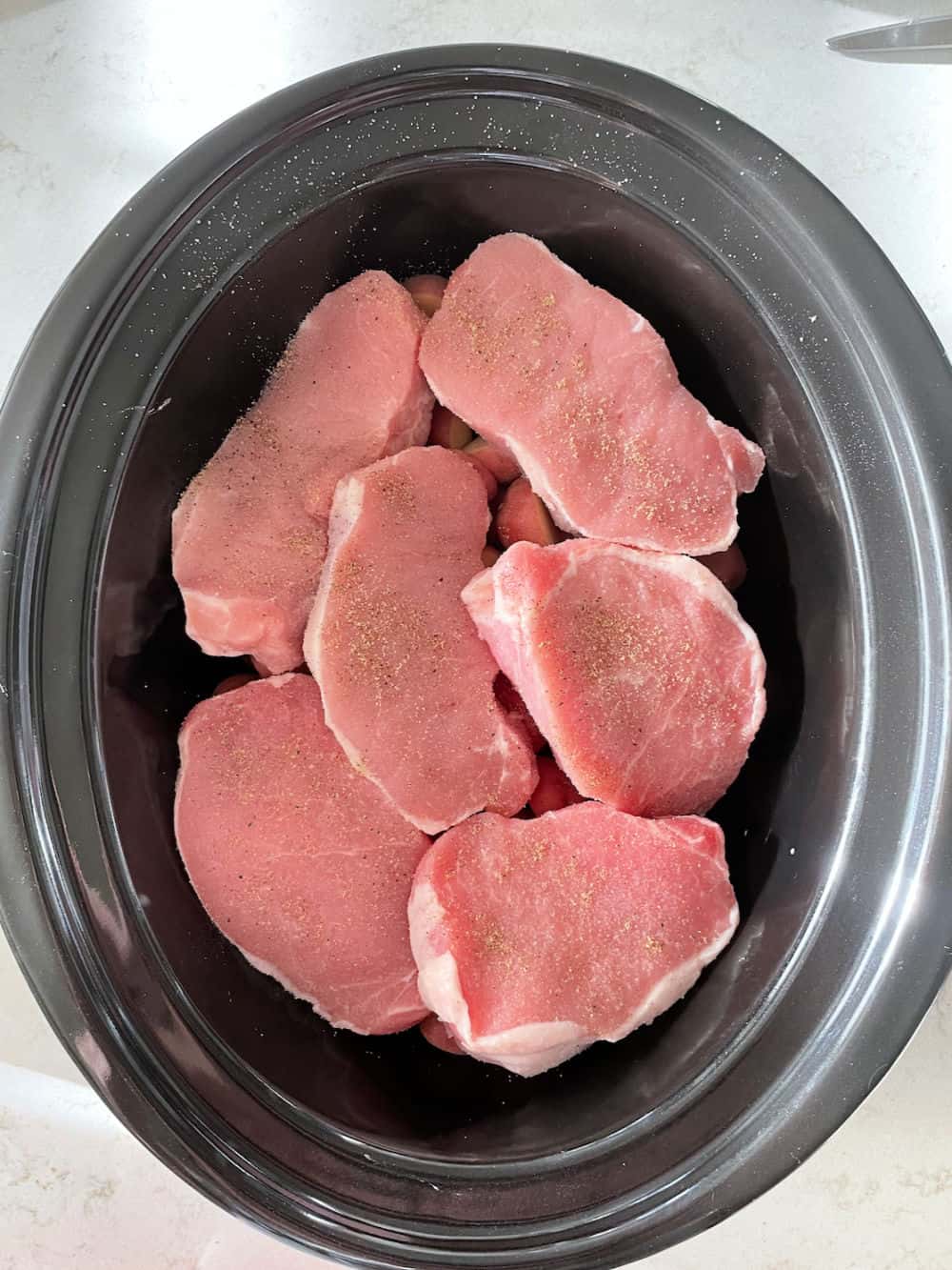 Pork Chops on top of potatoes in slow cooker