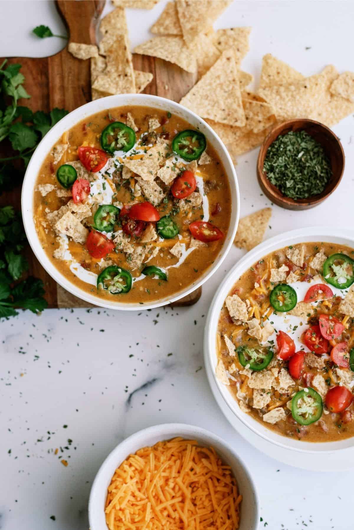 Slow Cooker Nacho Grande Soup in bowls with a side of shredded cheese and tortilla chips