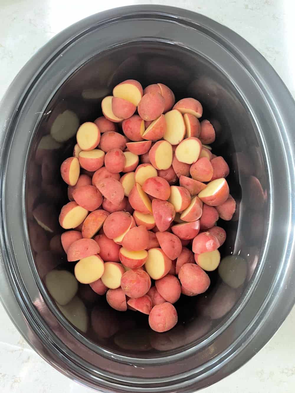 Potatoes sliced in half in bottom of slow cooker