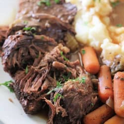Tender beef pot roast with carrots and mashed potatoes on a white plate.
