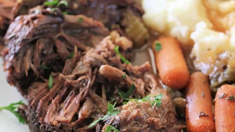 Tender beef pot roast with carrots and mashed potatoes on a white plate.