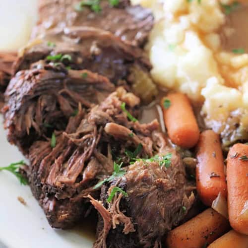 Tender beef pot roast with carrots and mashed potatoes on a white plate.