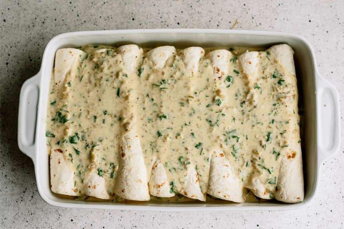 Unbaked Avocado Chicken Enchiladas in pan with sauce on top