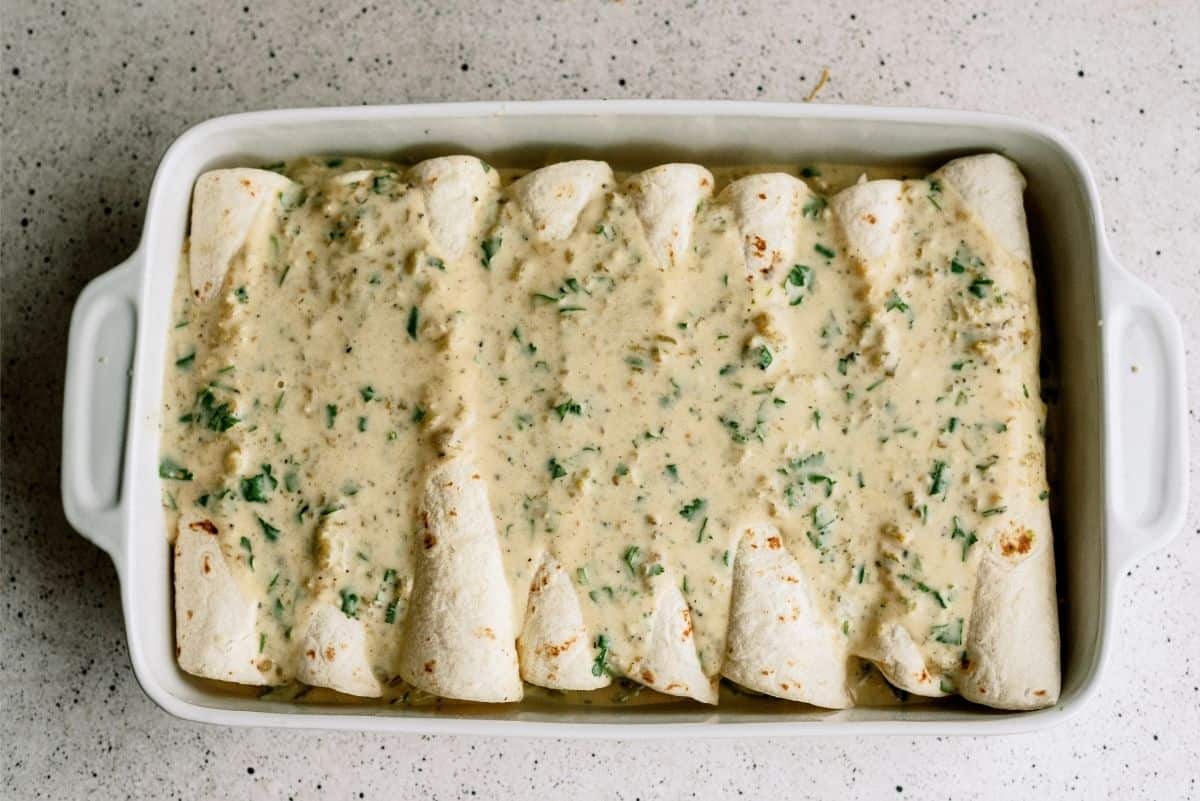 Unbaked Avocado Chicken Enchiladas in pan with sauce on top