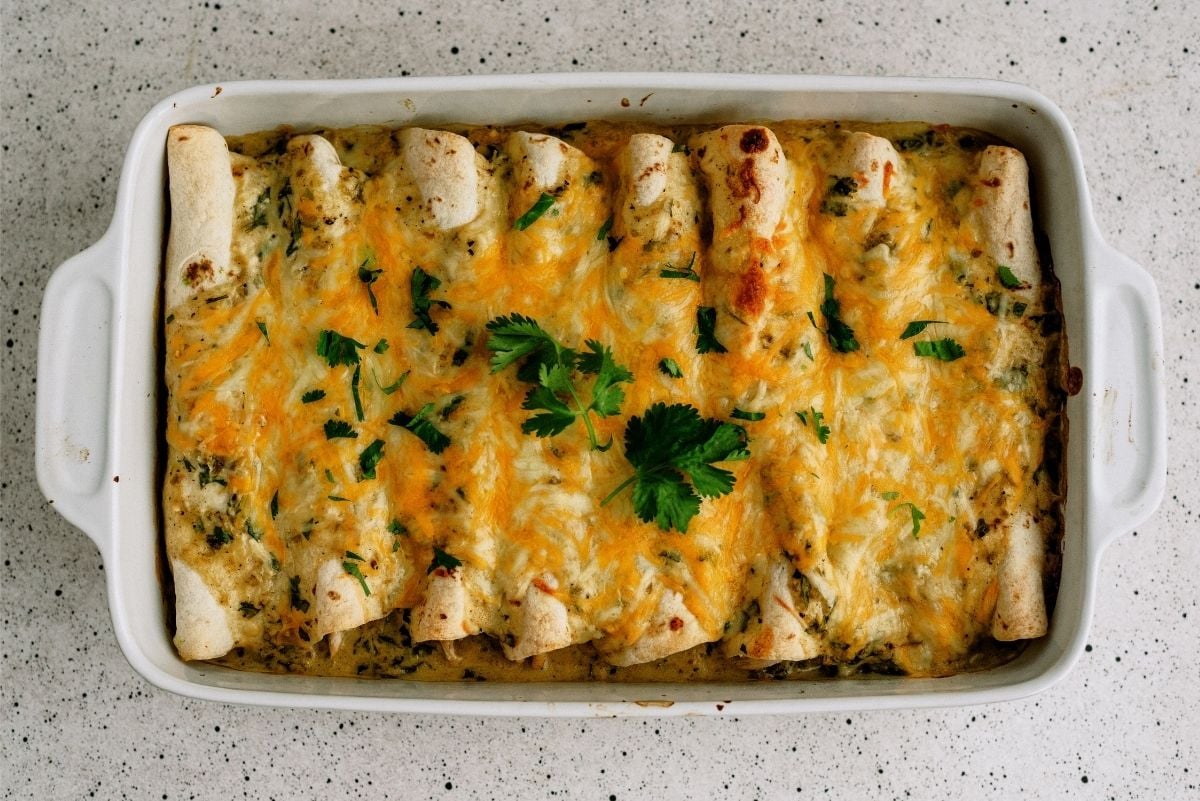 A pan of Avocado Chicken Enchiladas baked topped with cheese and cilantro