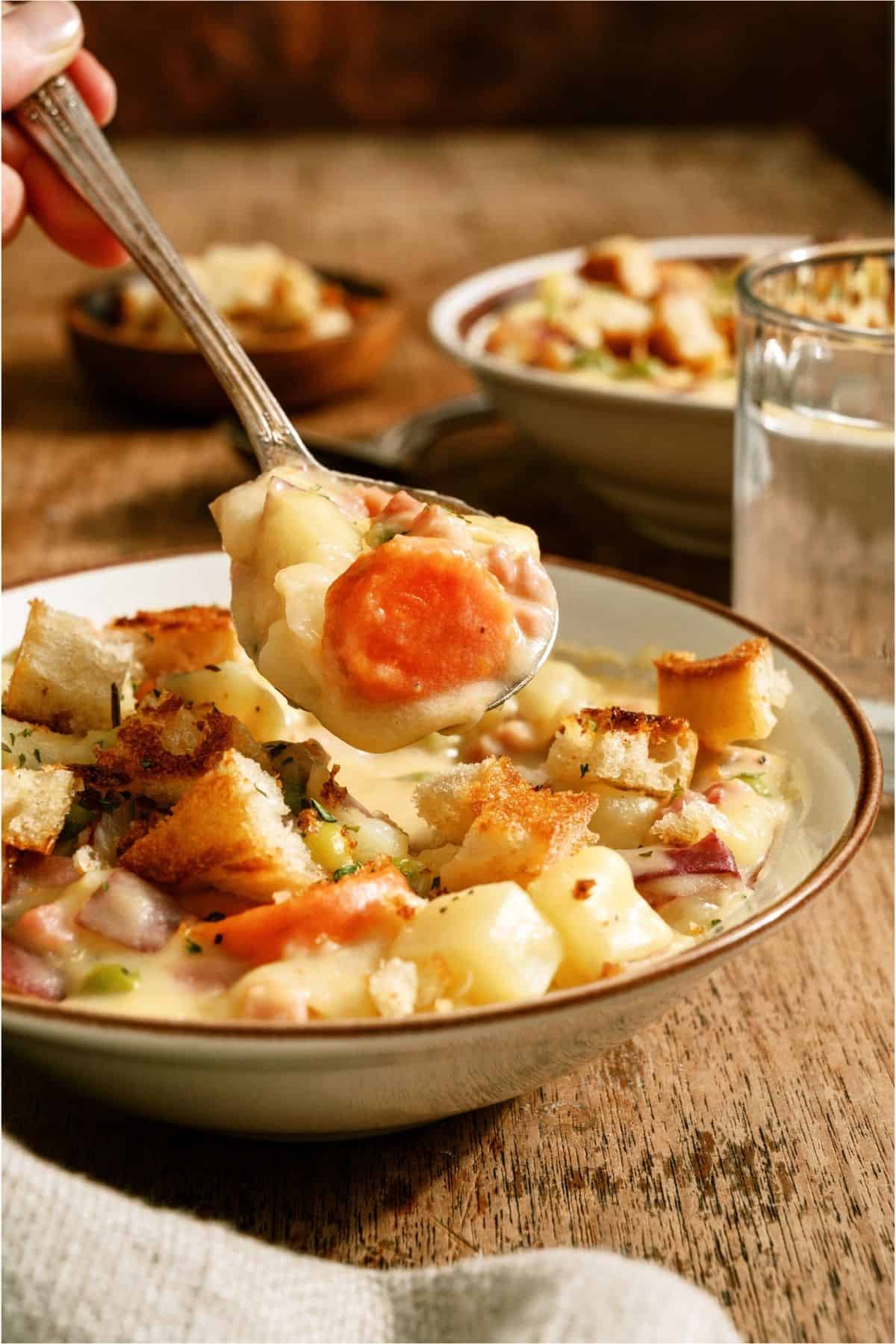 A spoon lifting a bite of Cheesy Ham and Potato Soup out of a bowl.
