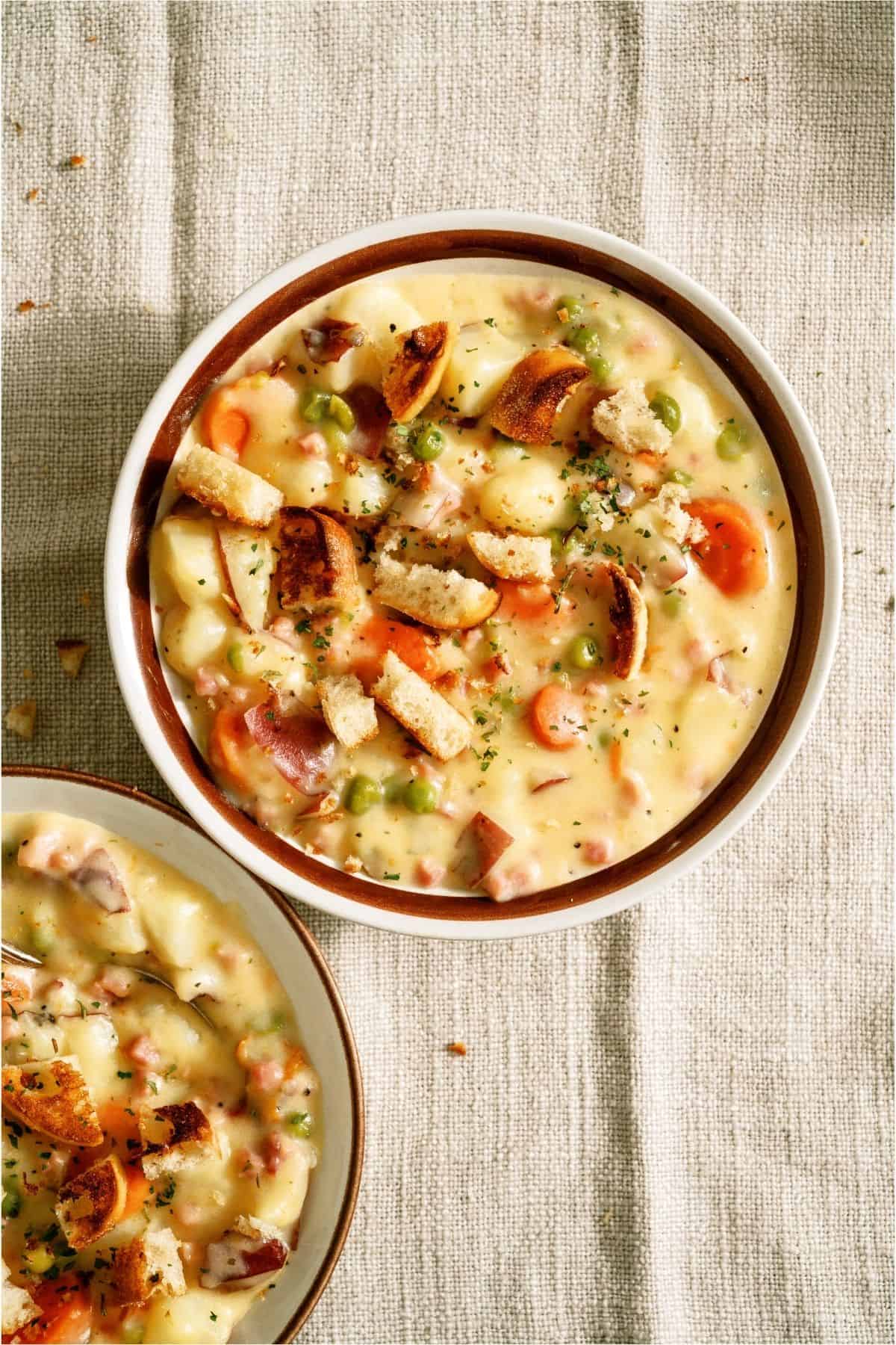 Top view of a bowl of Cheesy Ham and Potato Soup on a neutral background.