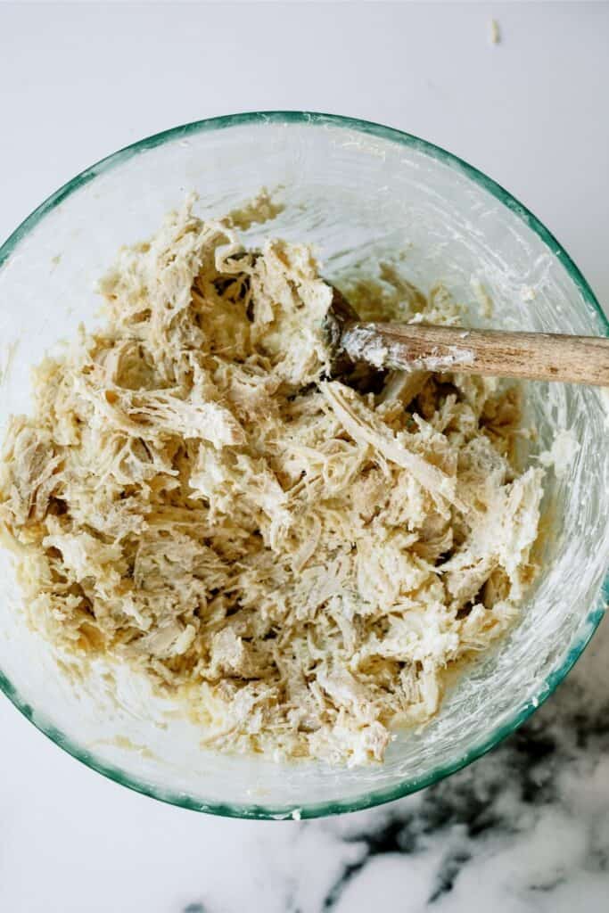 A glass bowl with shredded chicken and cheese.