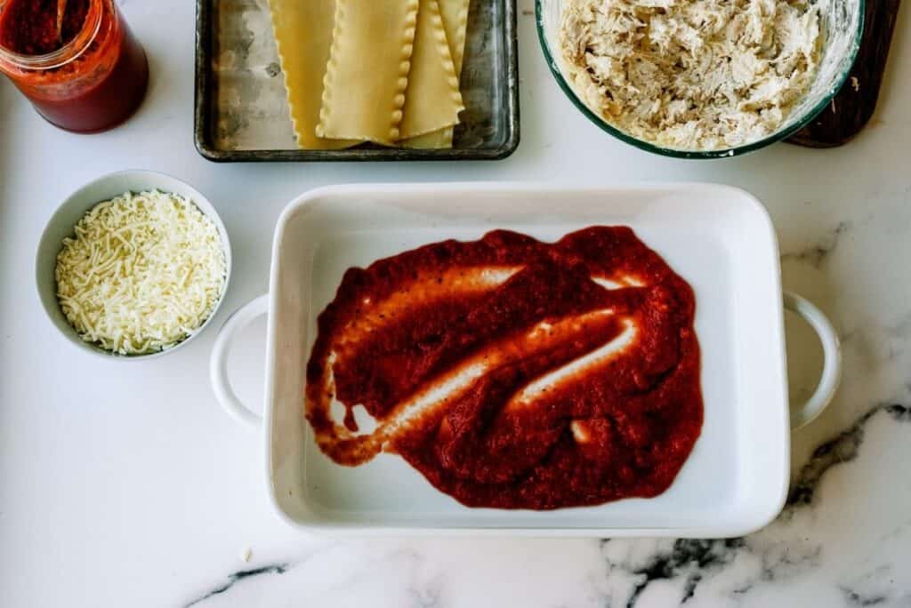 A casserole dish with pasta sauce in the bottom.