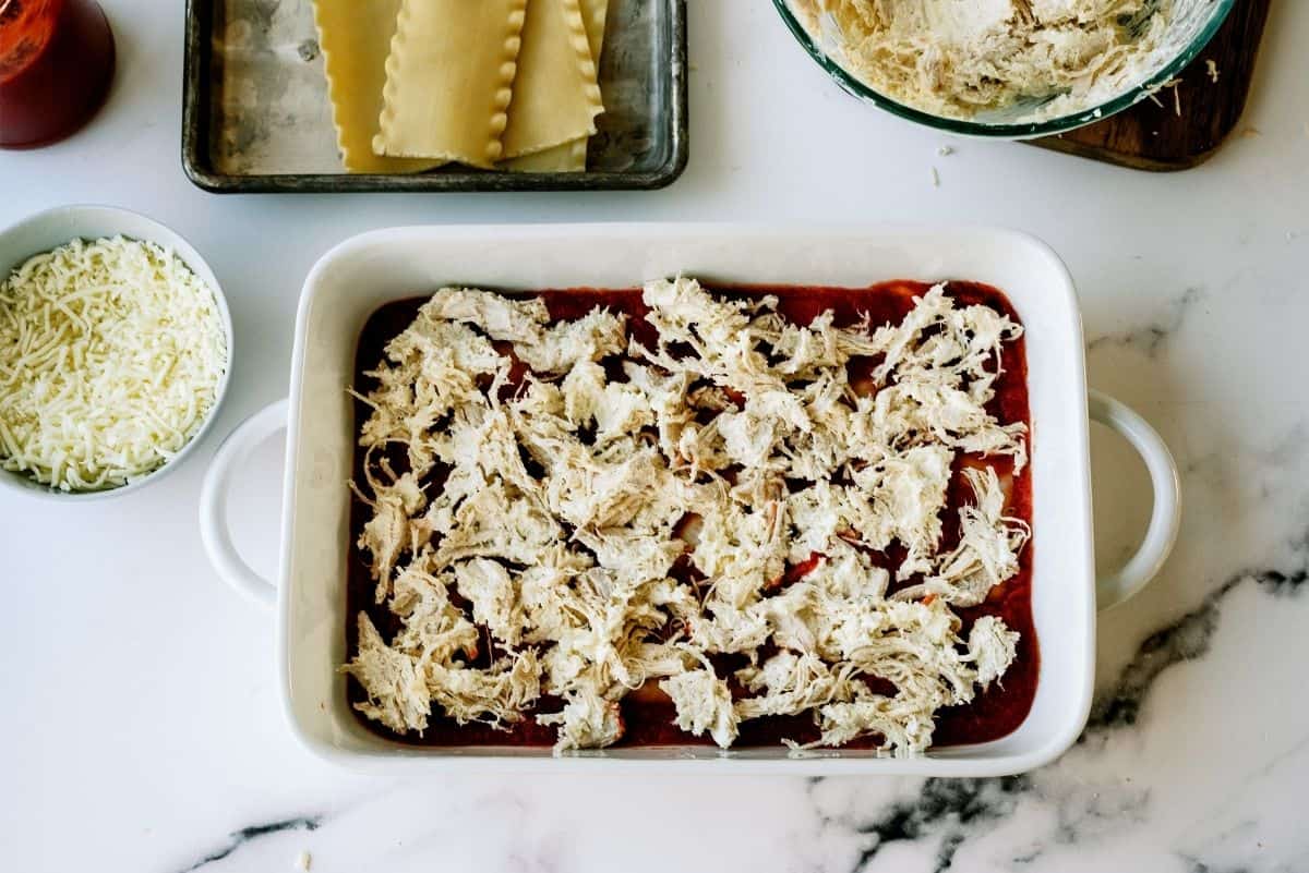 Shredded chicken mixture on top of spaghetti sauce in pan