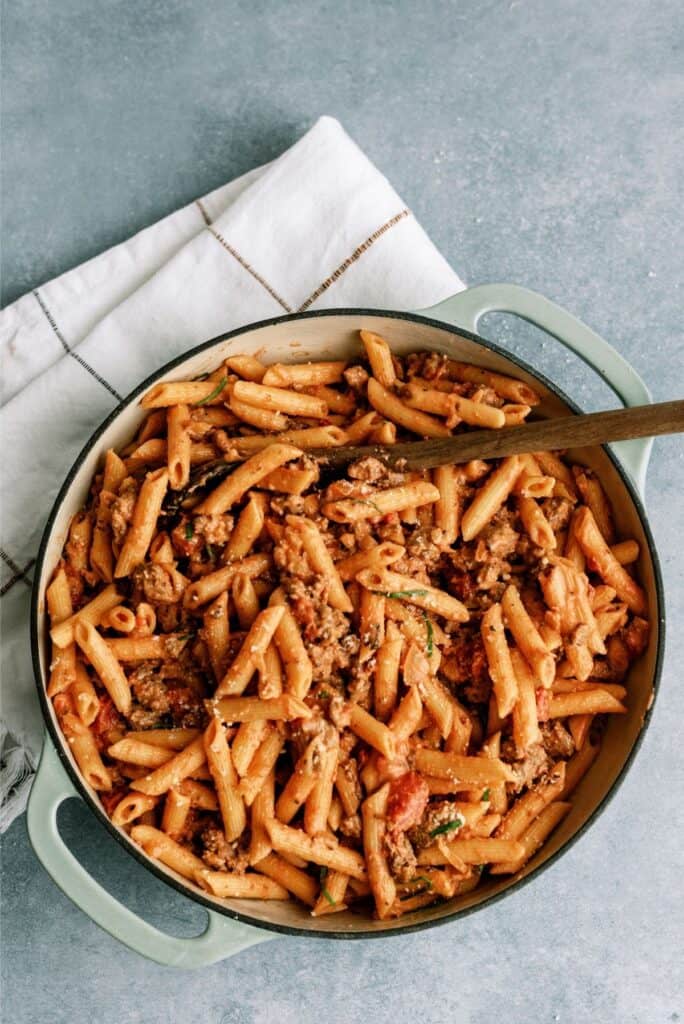 Top view of a pan of Creamy Sausage and Tomato Pasta with a wooden spoon.