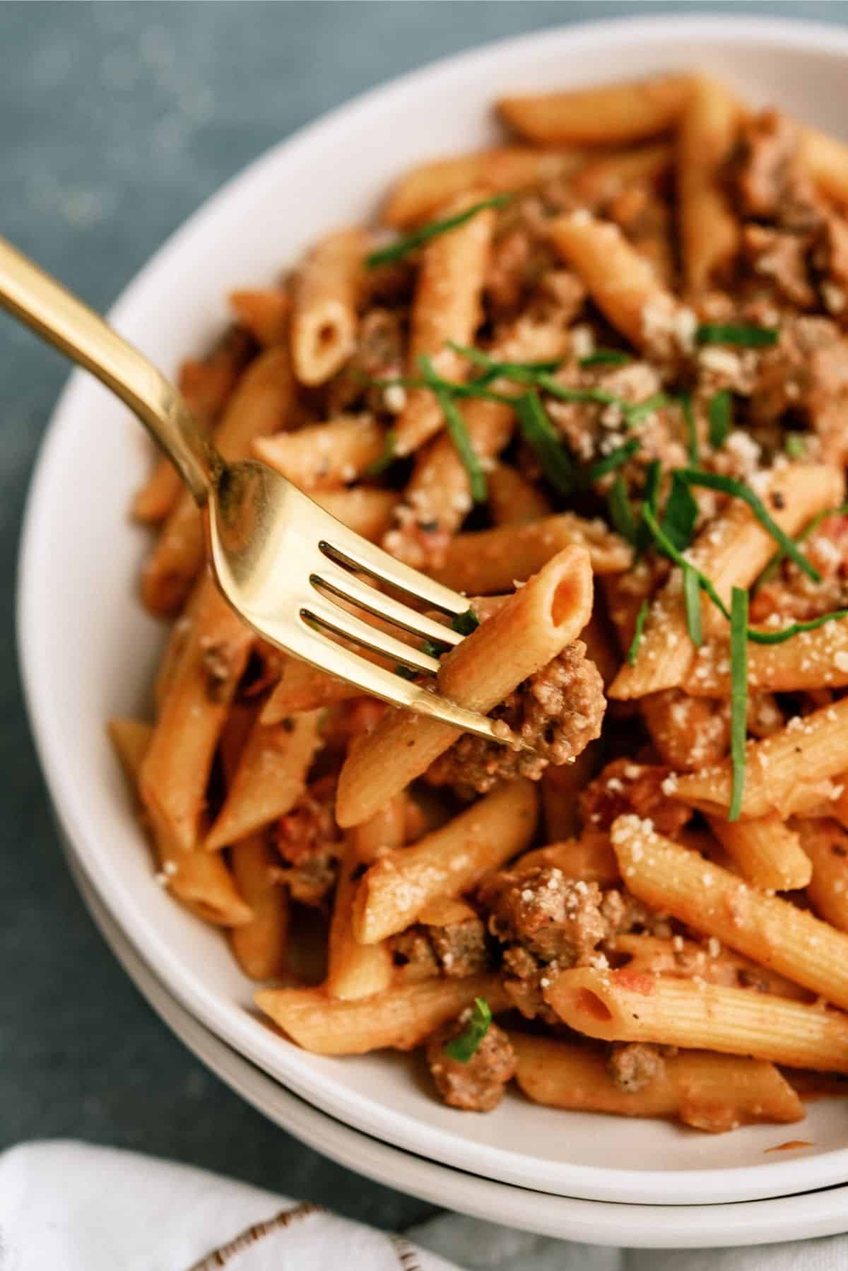 A fork lifting up a bite of Creamy Sausage and Tomato Pasta out of a bowl.