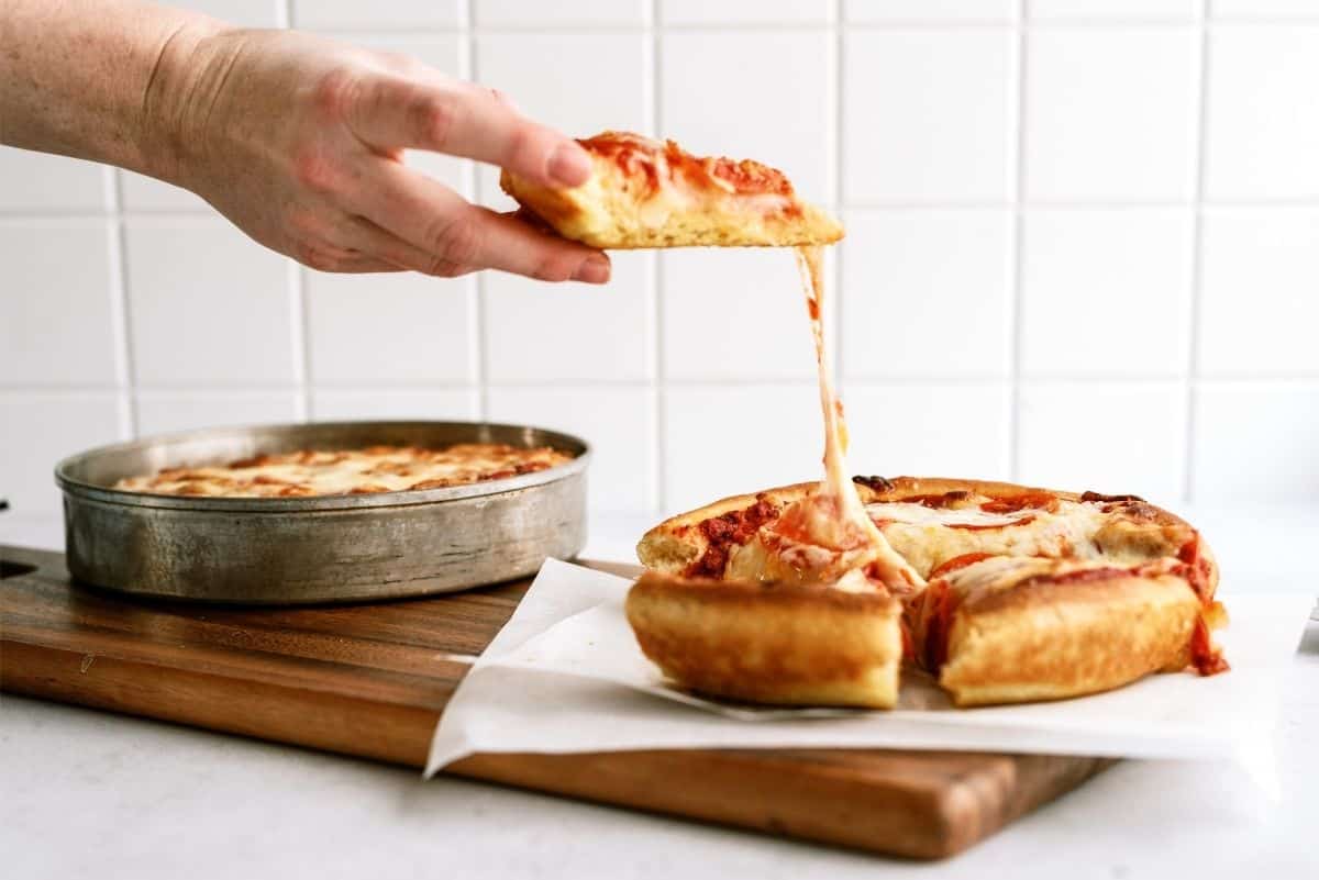 Slice of homemade pizza on a cutting board being grabbed from a big pizza pie