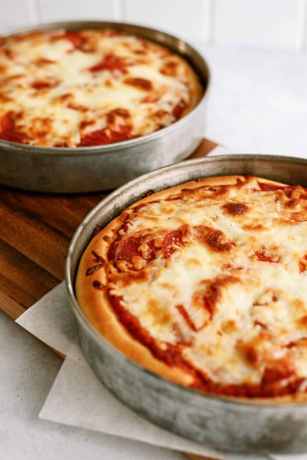 Homemade Pizza Hut Original Deep Dish Pizza in two cake pans sitting on a cutting board