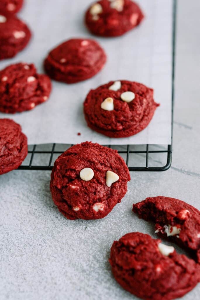 Red Velvet White Chocolate Chip Cookies on a cooling rack lined with parchment paper with 3 cookies on the counter.