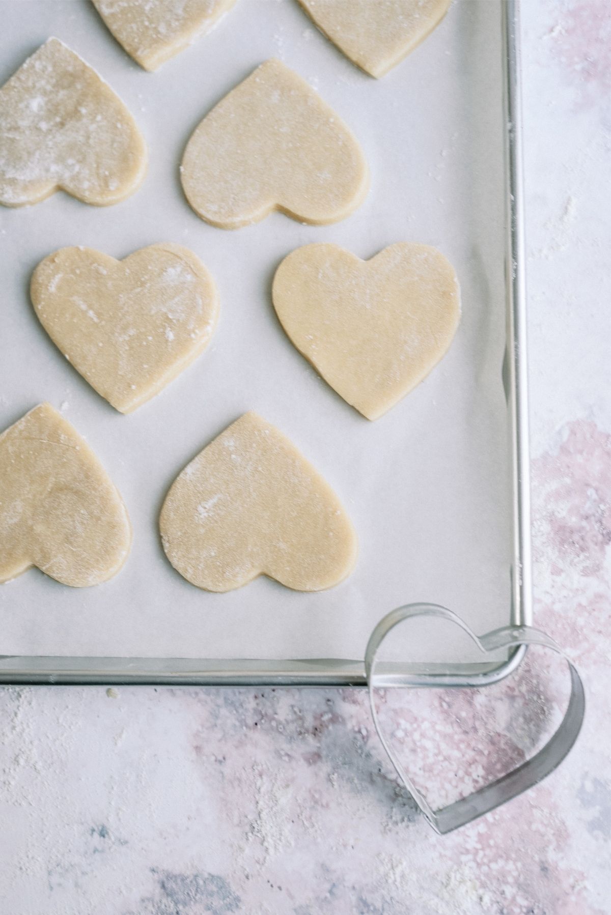 Unbaked heart shaped cookies on a baking sheet with heart shaped cookie cutter