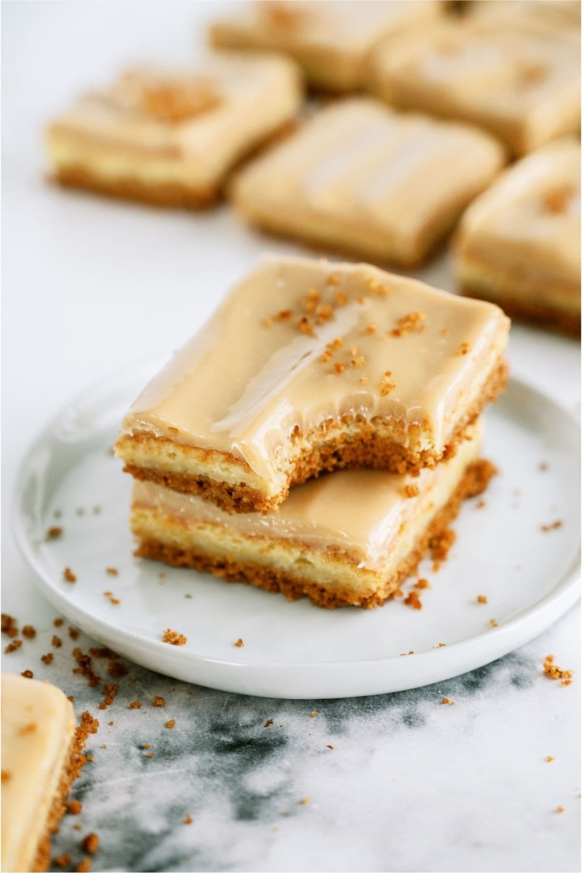 Two Caramel Cheesecake Bars stack on a plate with the top one missing a bite.