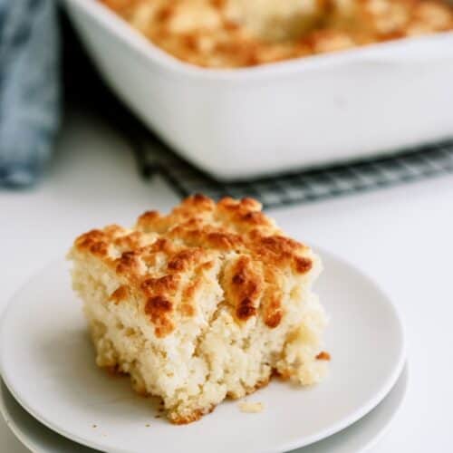 A serving of Pan Butter Biscuits on a plate with the remaining Pan Butter Biscuits in a baking dish in the background.