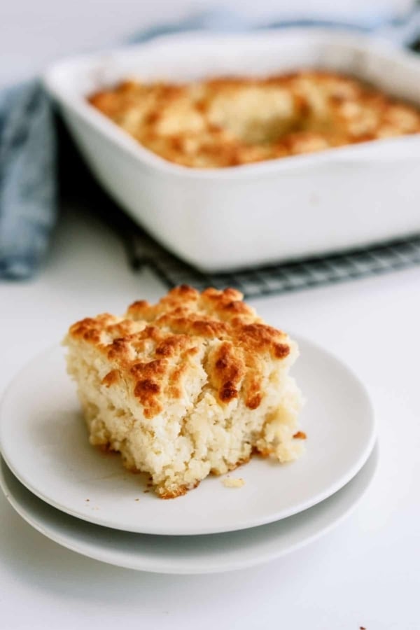 A serving of Pan Butter Biscuits on a plate with the remaining Pan Butter Biscuits in a baking dish in the background.