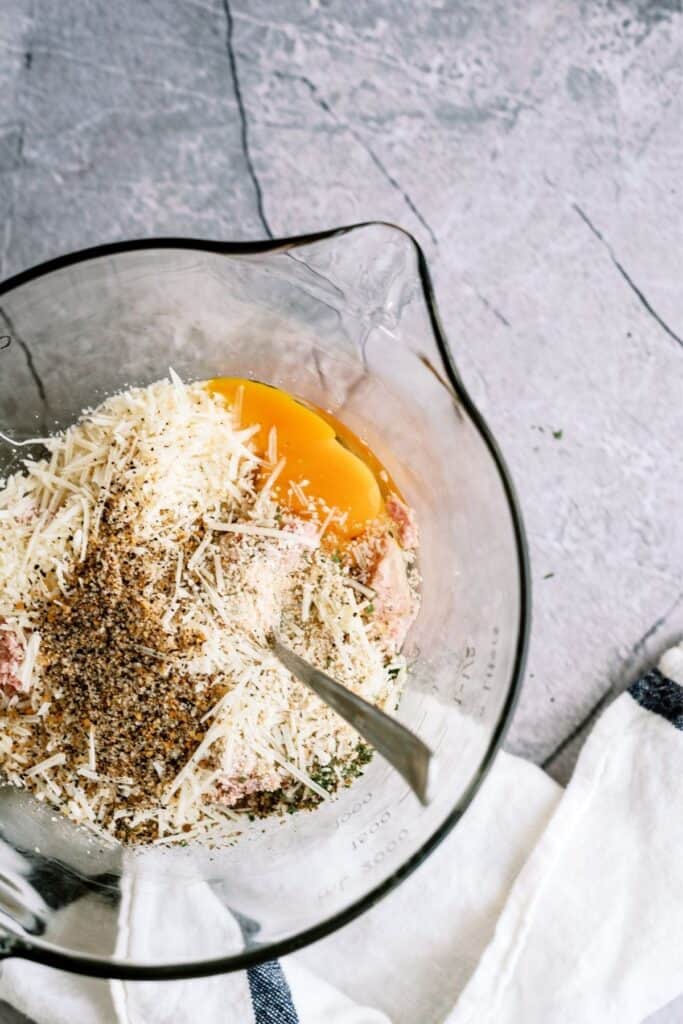 Mixing meatball ingredients in a glass mixing bowl.