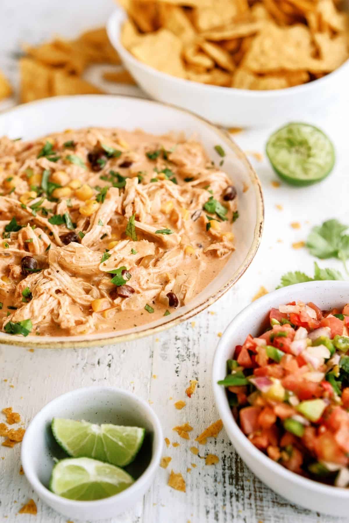 Instant Pot Creamy Fiesta Chicken in a bowl with chips, pico and limes on the side