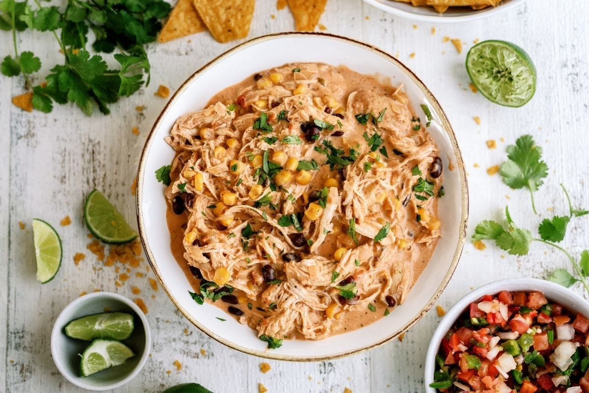 Instant Pot Creamy Fiesta Chicken in a bowl with pico, limes and chips on the side