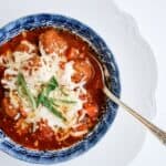 A bowl of meatball soup topped with cheese