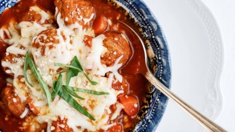 A bowl of meatball soup topped with cheese