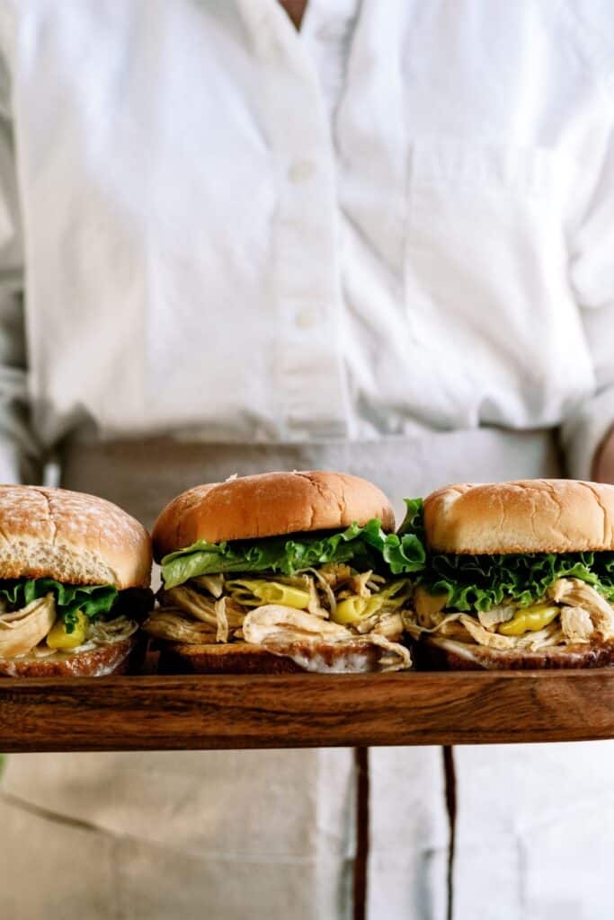 A chef holding 3 Instant Pot Mississippi Chicken Sandwiches.